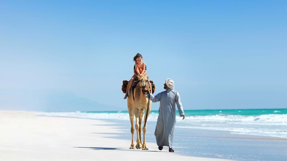 A girl enjoys a camel ride in a spectacular beach location at Al Baleed Resort Salalah by Anantara, Oman