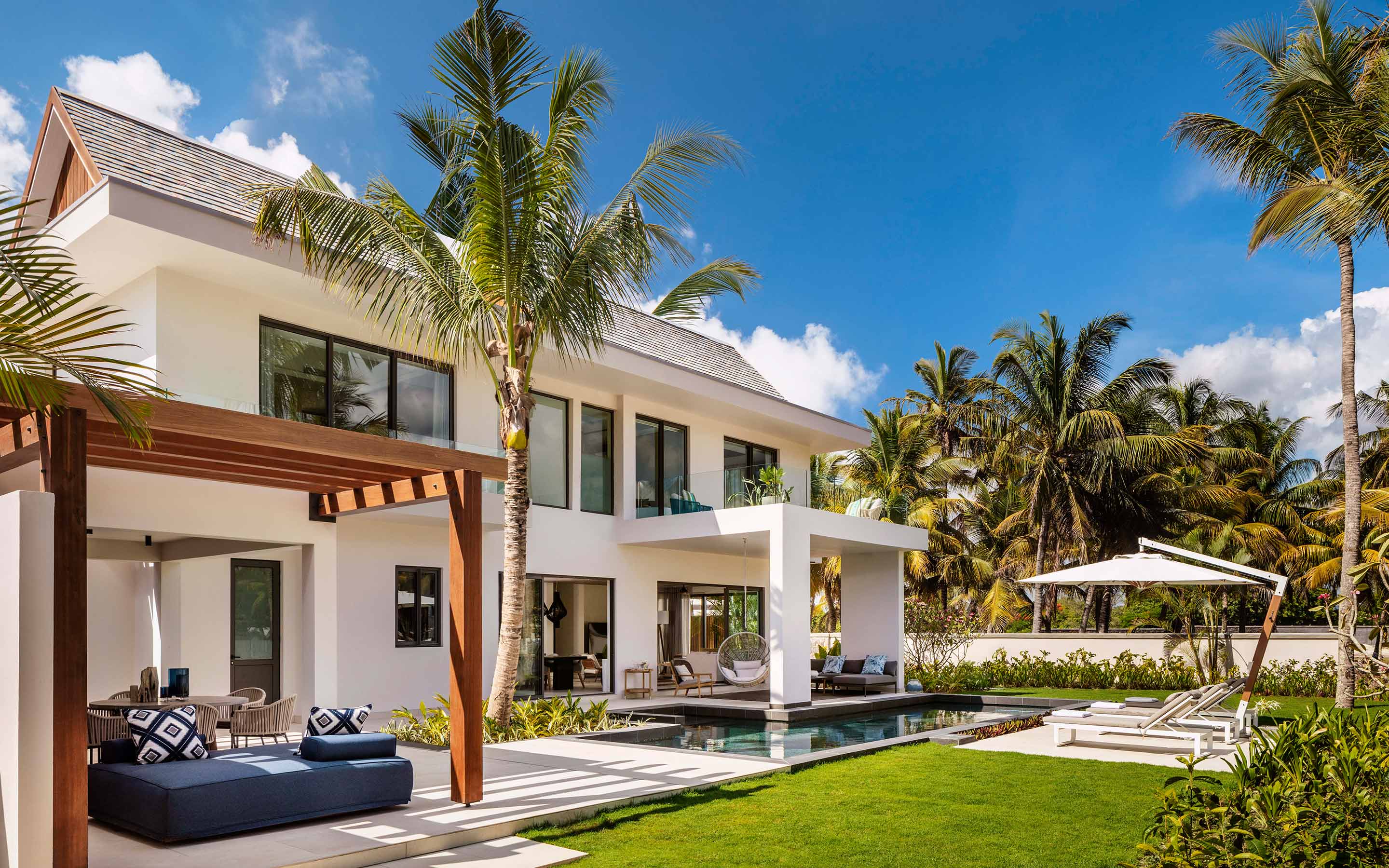 Pristine white pool cabanas sit just over the perfect clear water, beneath palm trees at One&Only Le Saint Geran, Mauritius